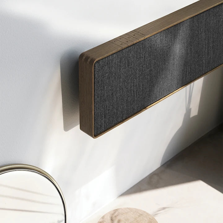 Beosound Stage soundbar monteret på hvid væg med træfinish og grå stofbetræk