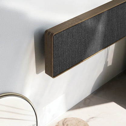 Beosound Stage soundbar monteret på hvid væg med træfinish og grå stofbetræk