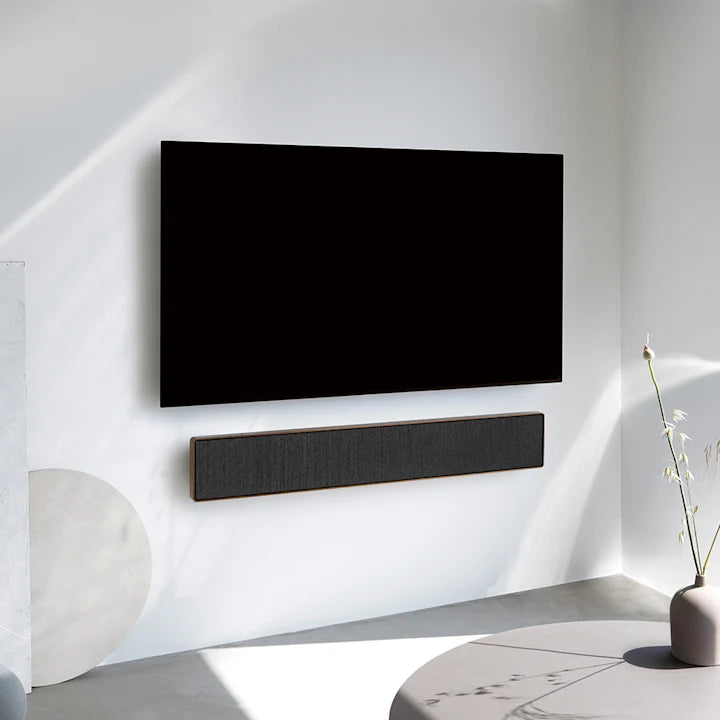 Beosound Stage soundbar monteret under sort fladskærms-tv på hvid væg i moderne stue