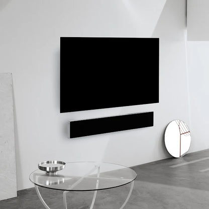 Beosound Stage soundbar monteret på hvid væg under fladskærms-TV med glassalontable i forgrunden
