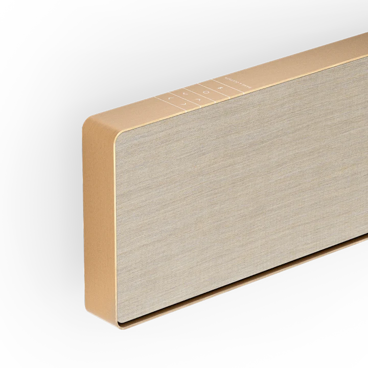 Beosound Stage soundbar i guldfarvet finish med lys stoffront, vist fra siden mod hvid baggrund