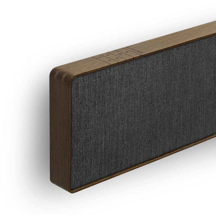 Beosound Stage soundbar i mørkt træ med grå stof, vist fra siden