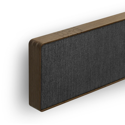 Beosound Stage soundbar i mørkt træ med grå stof, vist fra siden